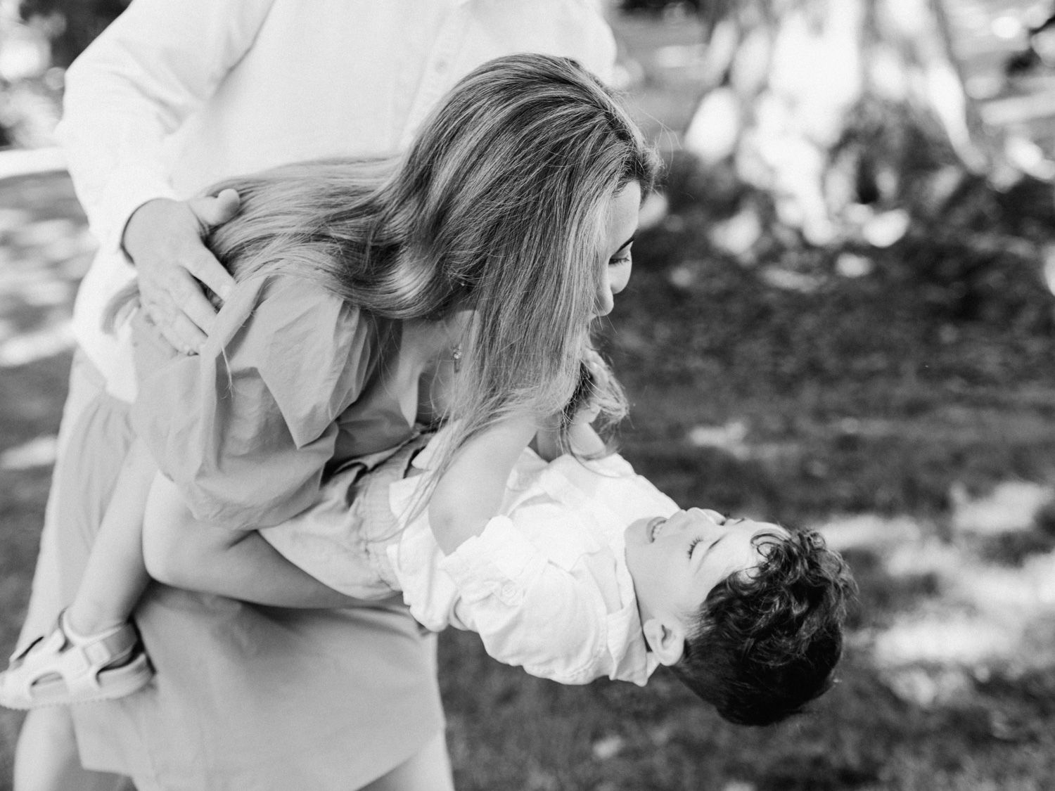 Black and white photo of a woman lovingly holding and leaning over a young child outdoors in a garden.