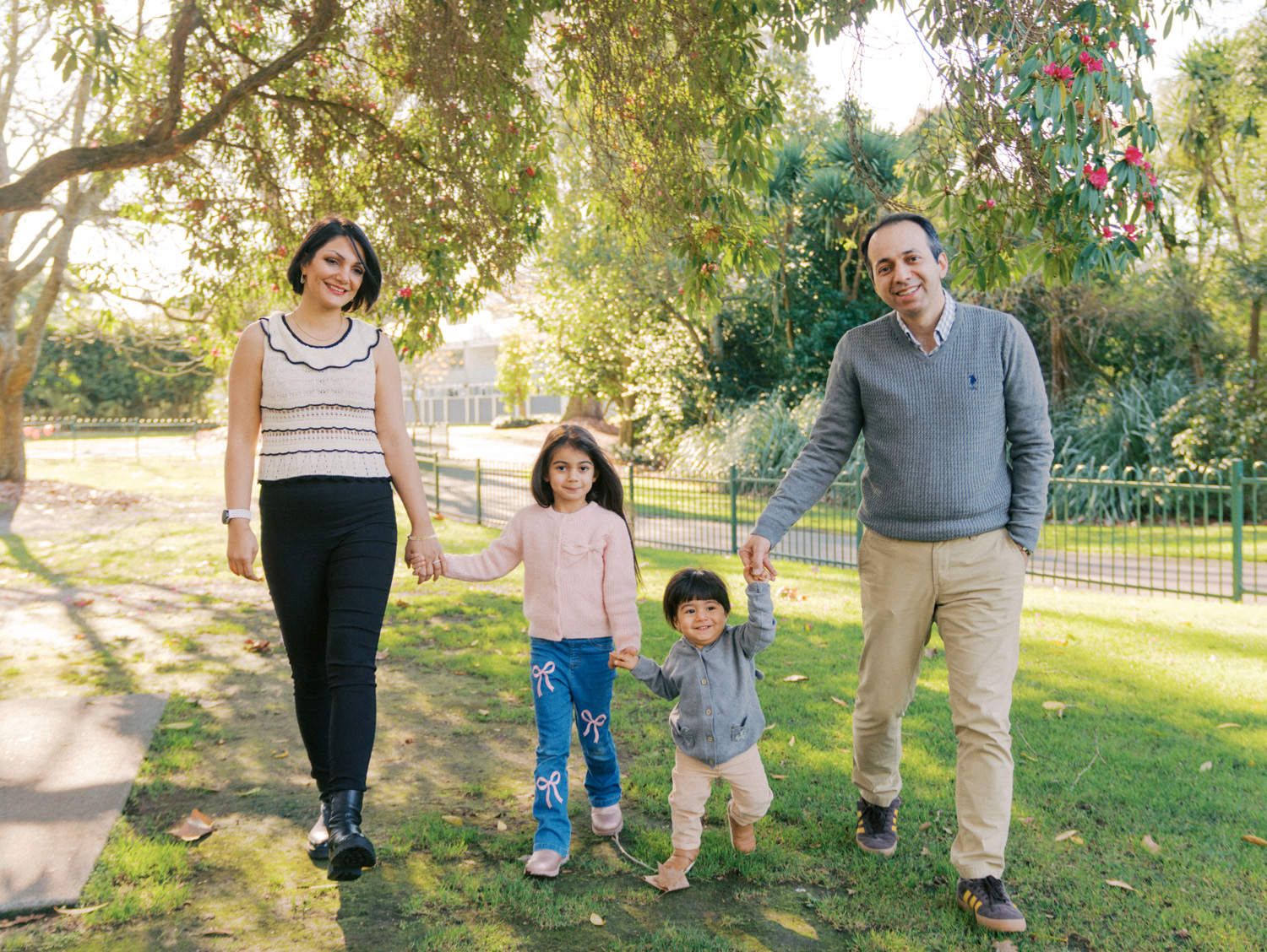 Happy family of four holding hands walking in a sunny green park on a beautiful day.