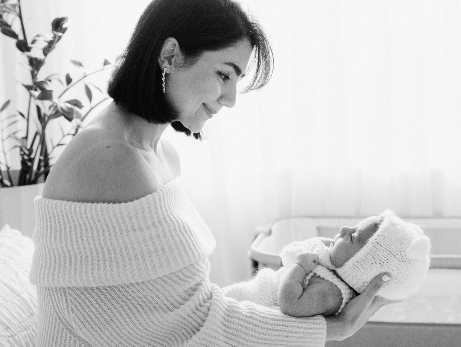 Black and white photo of a mother in off-shoulder sweater lovingly gazing at her newborn.