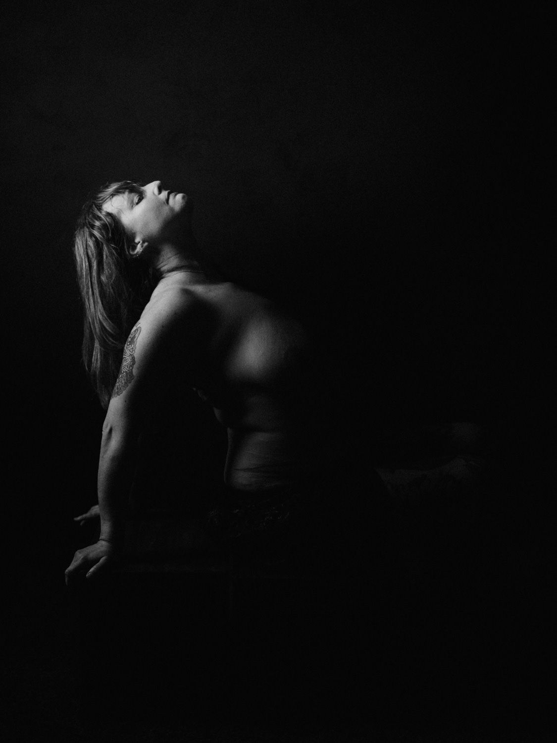Black and white fine art photo of a woman arching her back dramatically against a dark background.