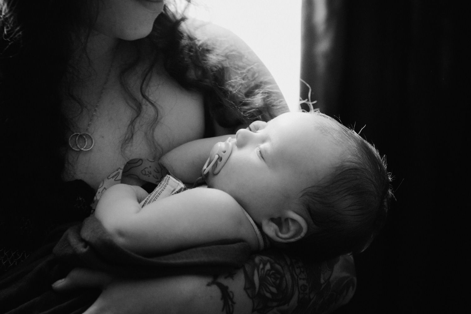 Black and white photo of a mother tenderly cradling her sleeping newborn baby in her arms.
