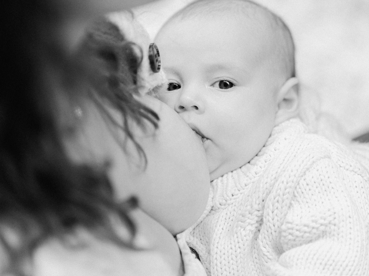 Black and white photo of a mother tenderly kissing her newborn baby in a soft knit sweater.