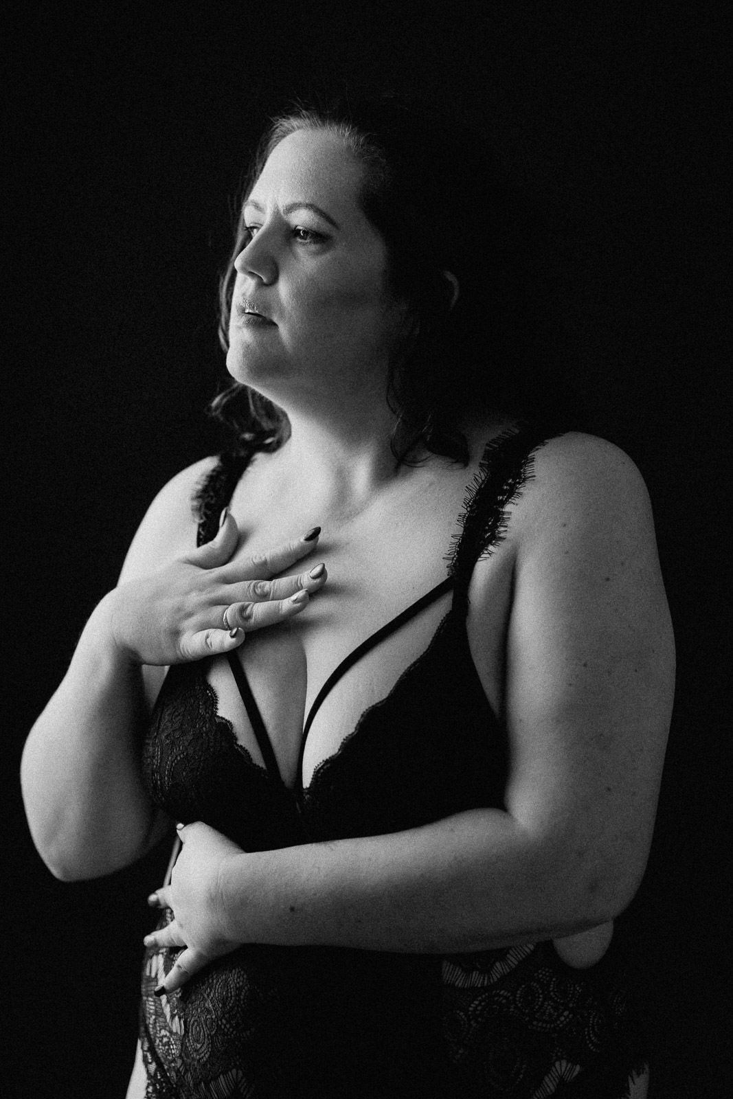 Black and white portrait of a woman in lace lingerie posing against a dark background.