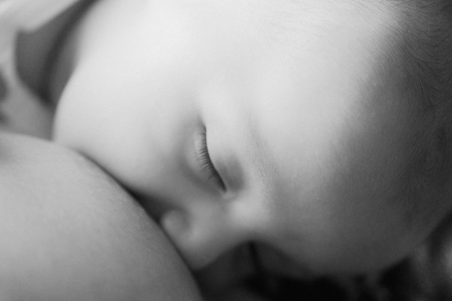 Close-up black and white photo of a sleeping newborn baby with delicate eyelashes and peaceful expression.