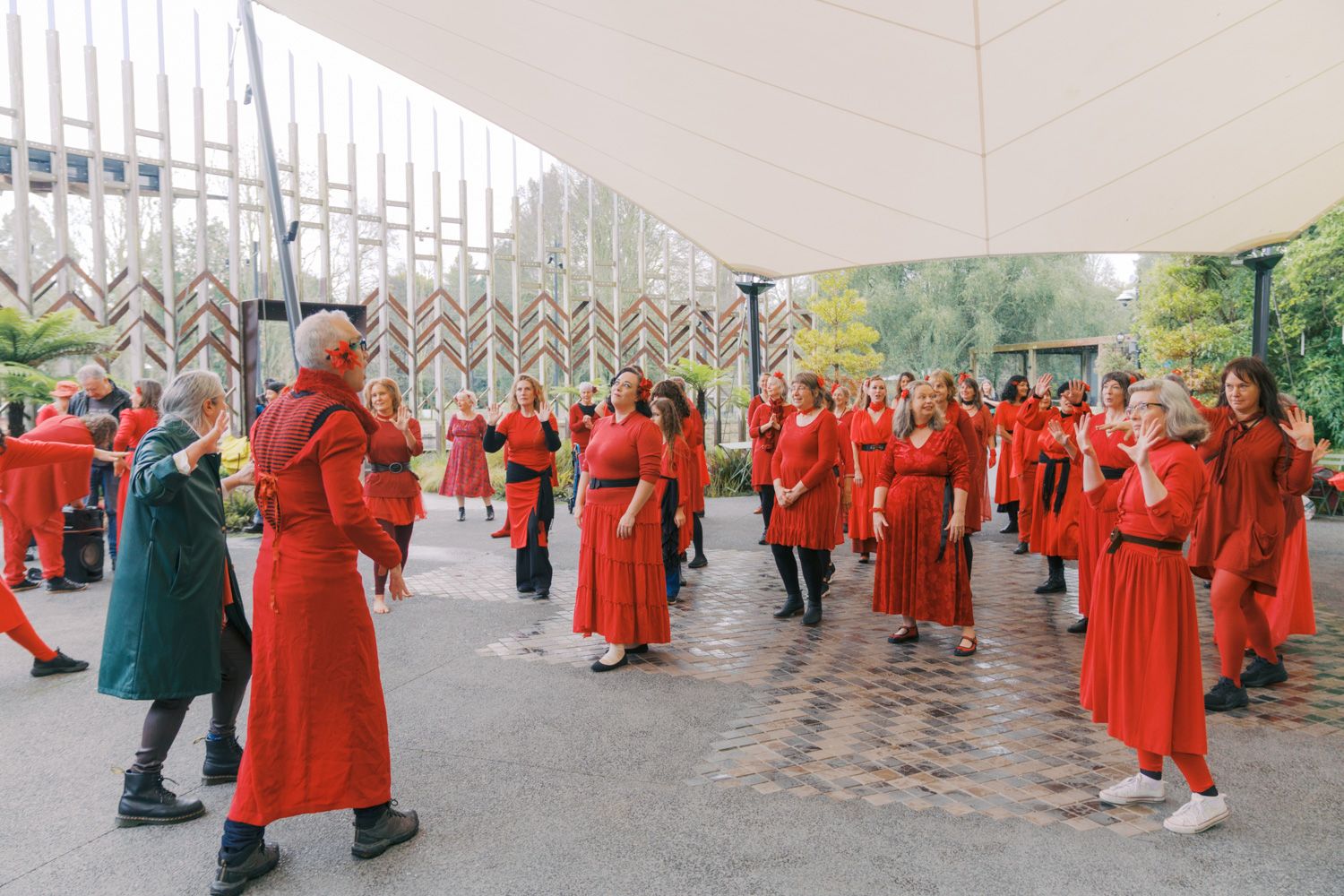 Large group of people dressed in red costumes gathered outdoors under a canopy at a cultural event.