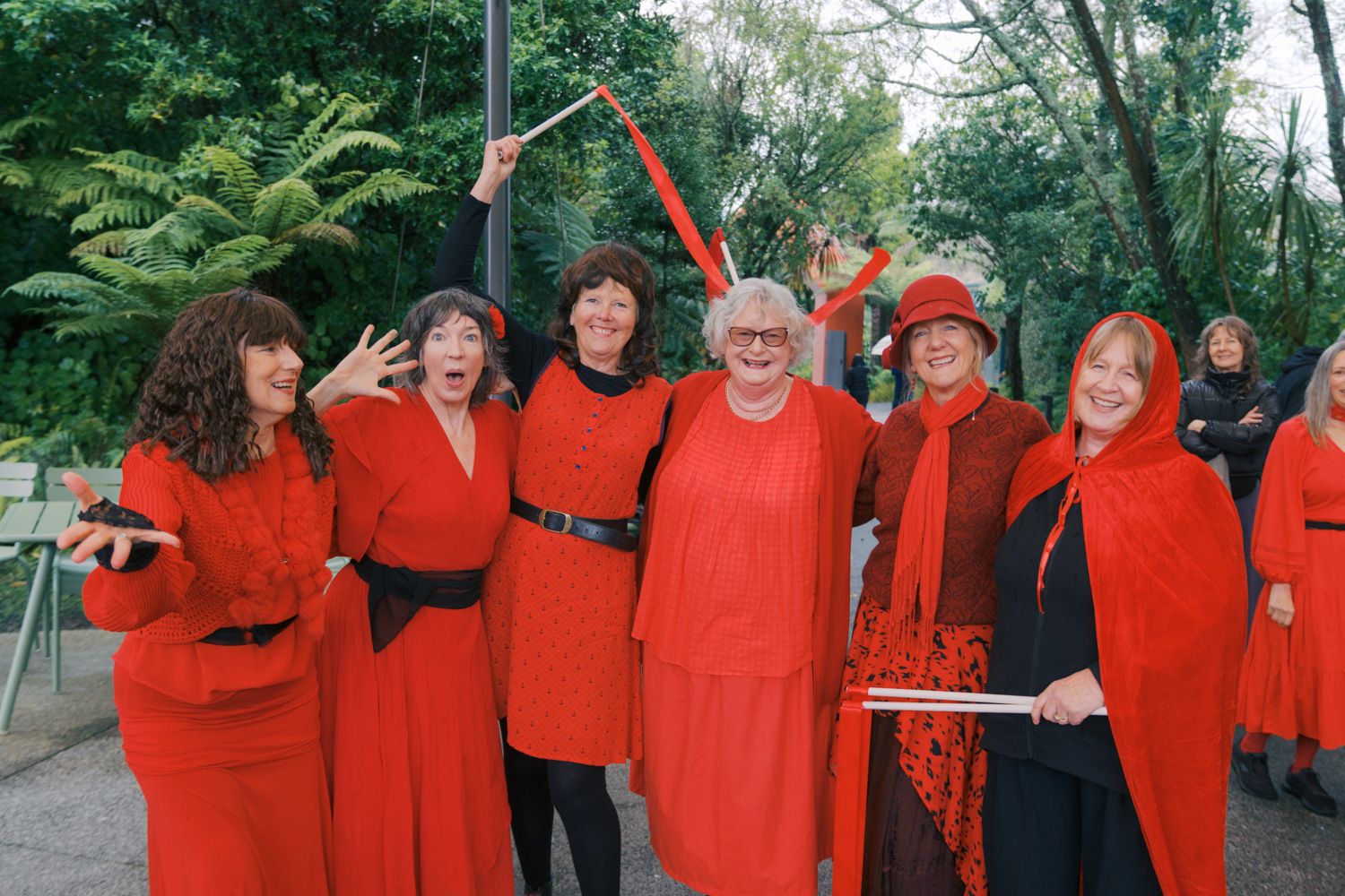 Group of women dressed in red robes and hats posing together outdoors at a festive gathering.