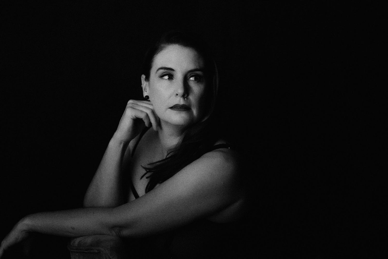 Black and white portrait of a young woman resting her chin on her hand against a dark background.