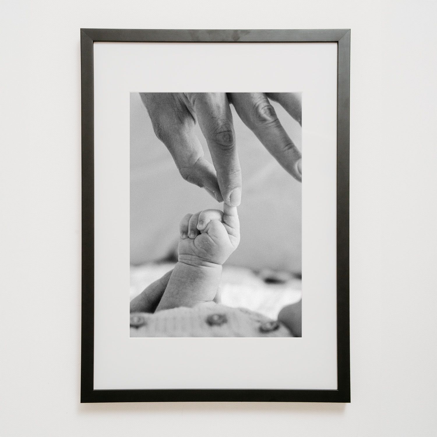 Black and white framed photo of a newborn baby's tiny hand grasping an adult's finger, symbolizing new life and parental bond.