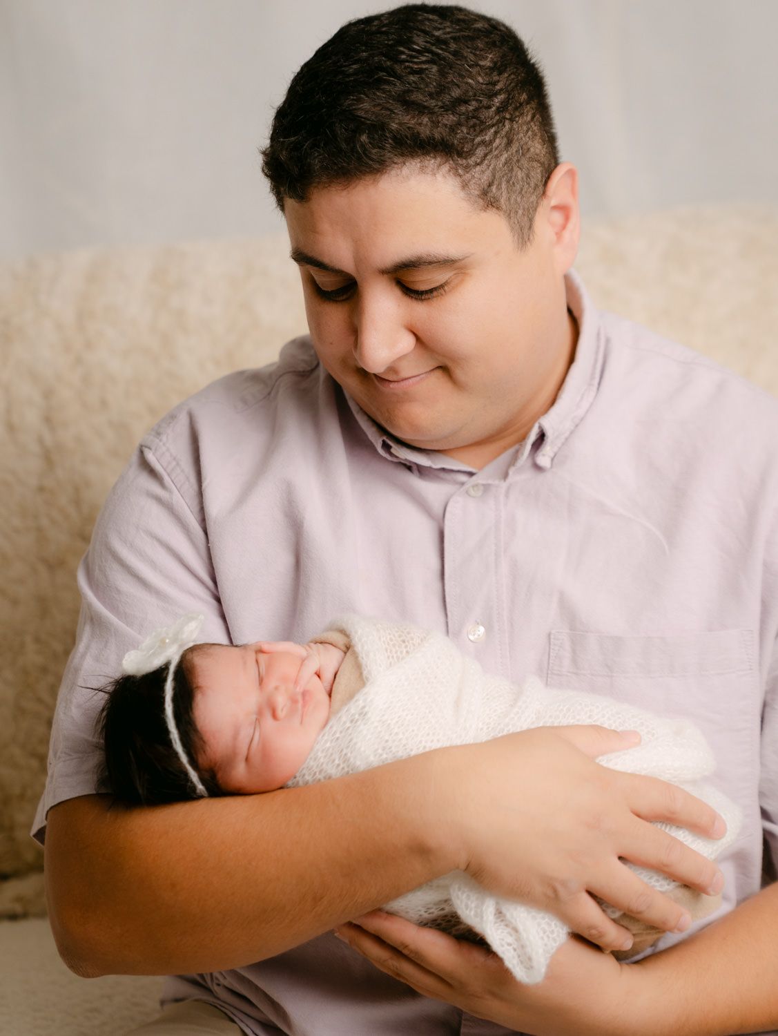 A proud father tenderly holds his swaddled newborn baby during a professional studio portrait session.