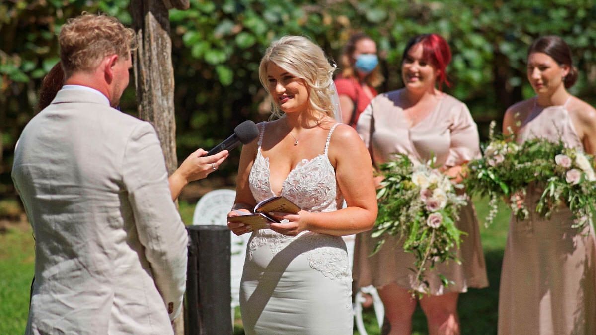 Bride reads vows to groom at outdoor wedding ceremony with bridesmaids holding floral bouquets in background.
