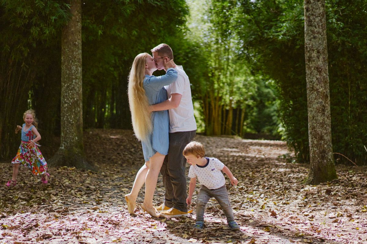 A loving couple shares a kiss in a bamboo forest while their two young children play nearby.