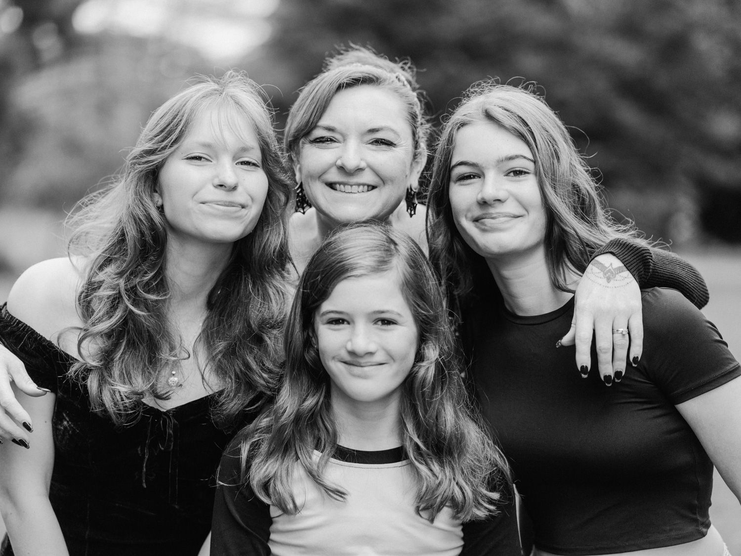 Black and white portrait of four smiling girls posing together outdoors in a candid family photo.