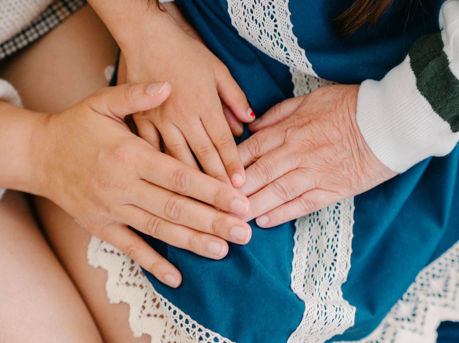 Three generations of hands resting together on a blue dress, symbolizing family bond and love.