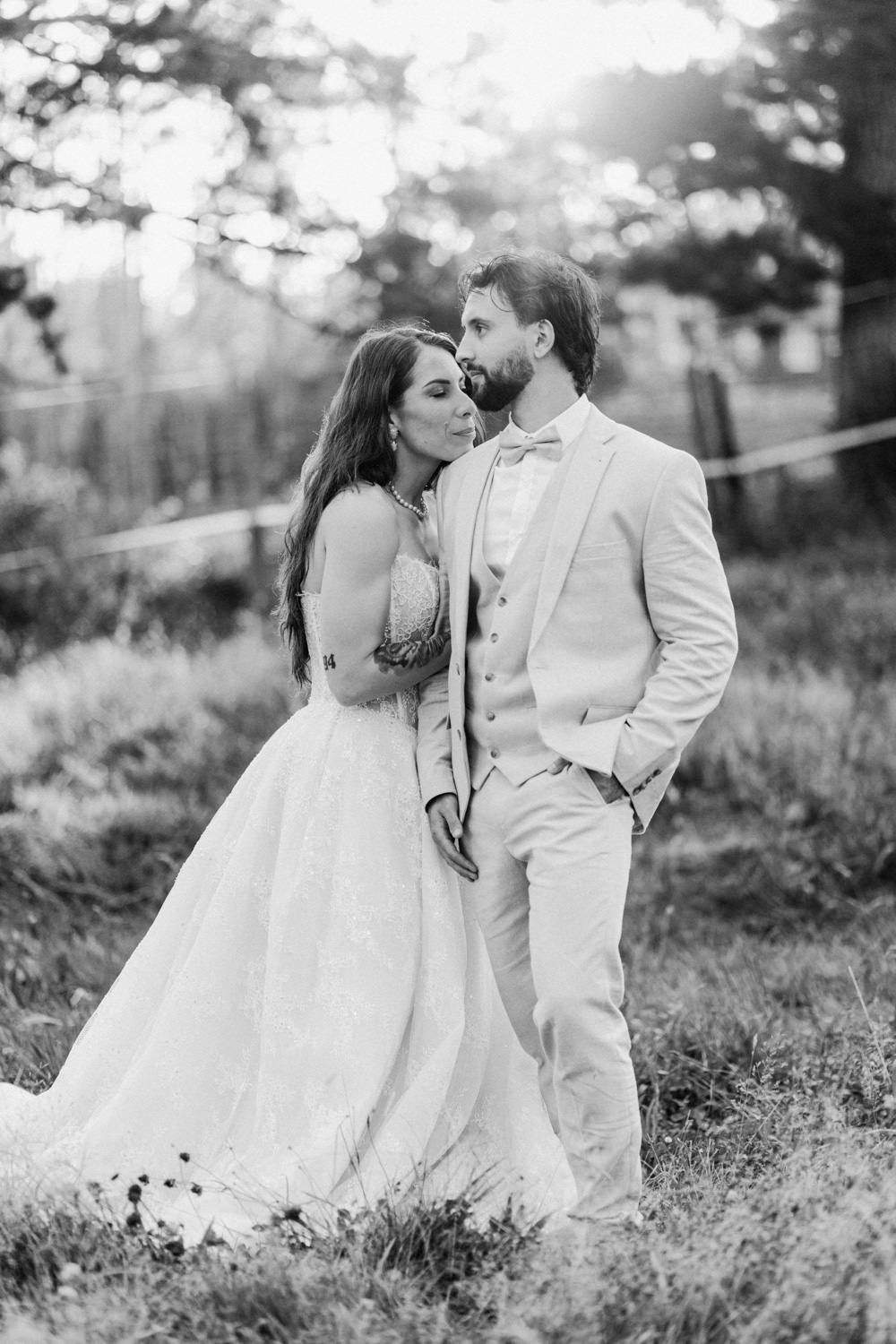 Black and white photo of a bride and groom embracing outdoors, with soft bokeh lighting in the background.