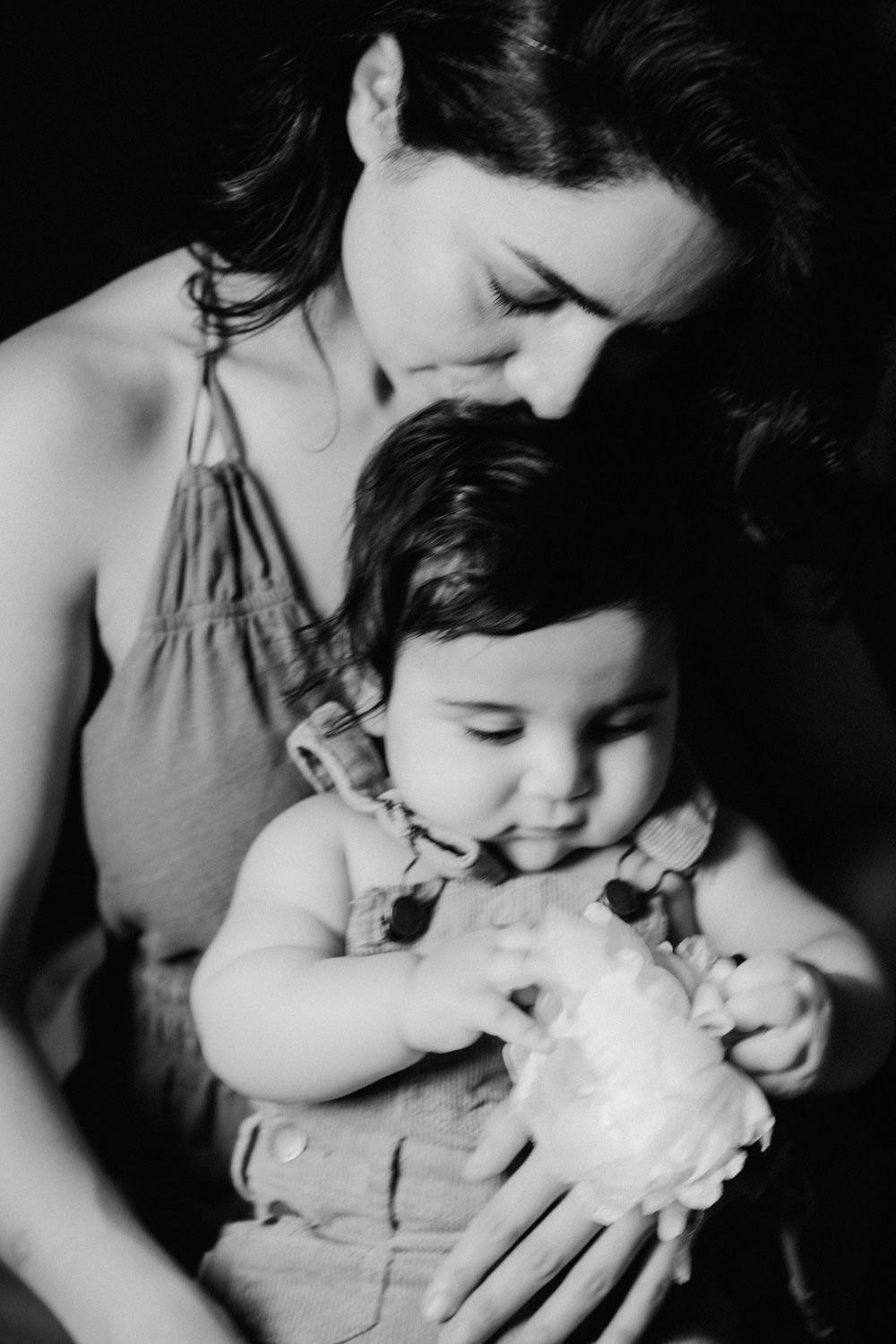 Black and white photo of a mother tenderly holding her baby who clutches a white flower.