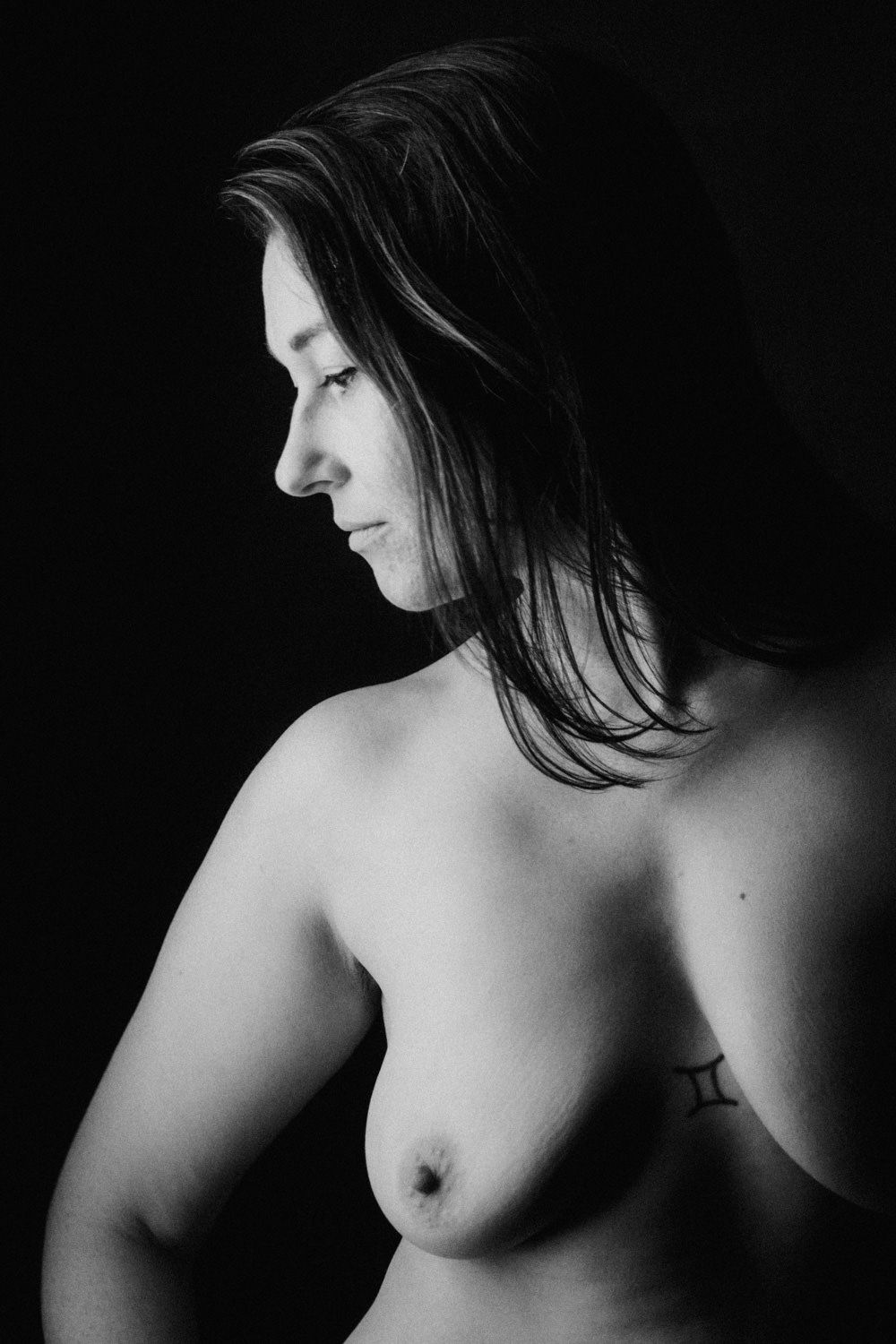 Black and white profile portrait of a woman with flowing hair, artistic nude photography with dramatic lighting.