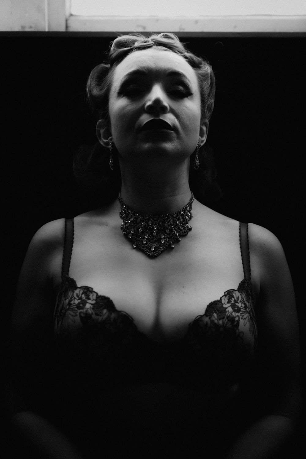 Black and white portrait of woman in lace top with ornate choker necklace, dramatic lighting.