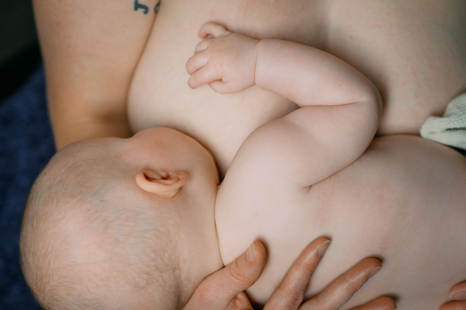 Newborn baby breastfeeding, cradled in mother's arms in a natural, intimate nursing moment.