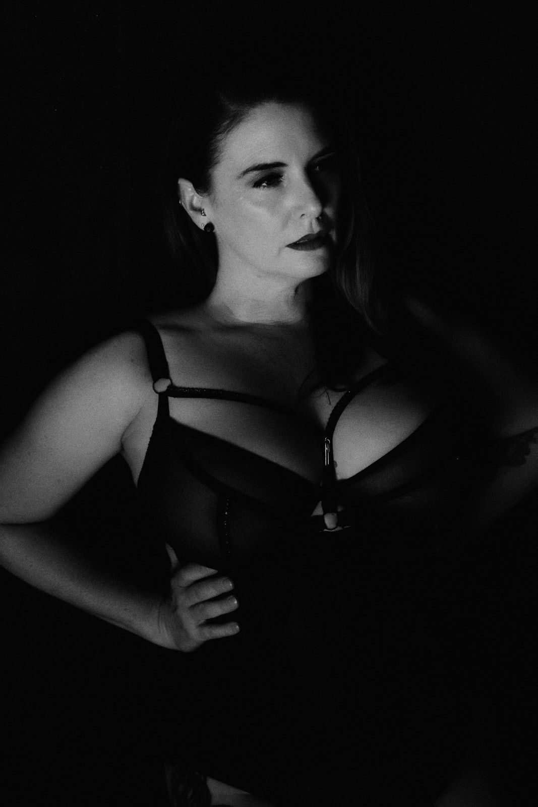 Black and white boudoir portrait of a woman in lingerie posing confidently against a dark background.