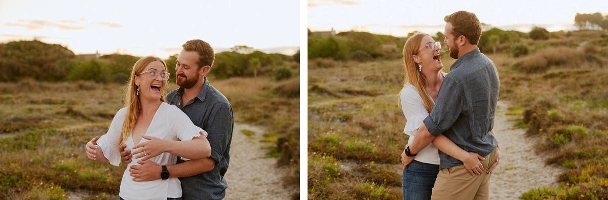 Happy couple laughing and embracing outdoors in golden hour light among coastal scrubland vegetation.
