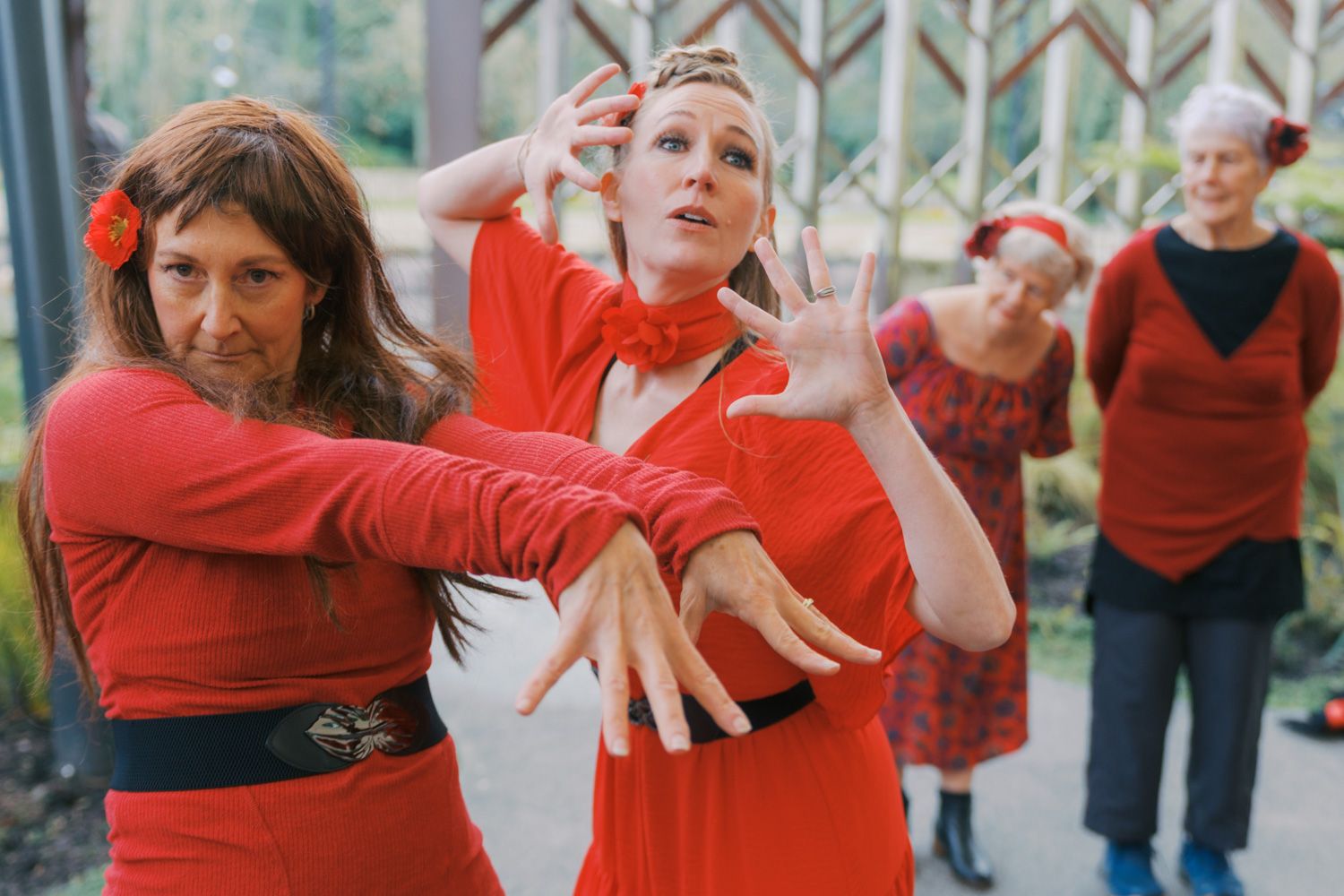 Women in red dresses perform expressive dance movements outdoors in a vibrant group performance.