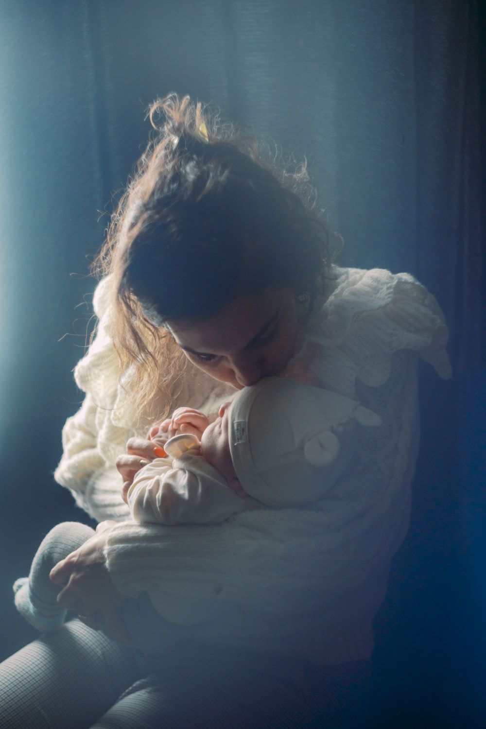 Young girl hugging a soft stuffed animal toy by a sunlit window in warm white clothing.