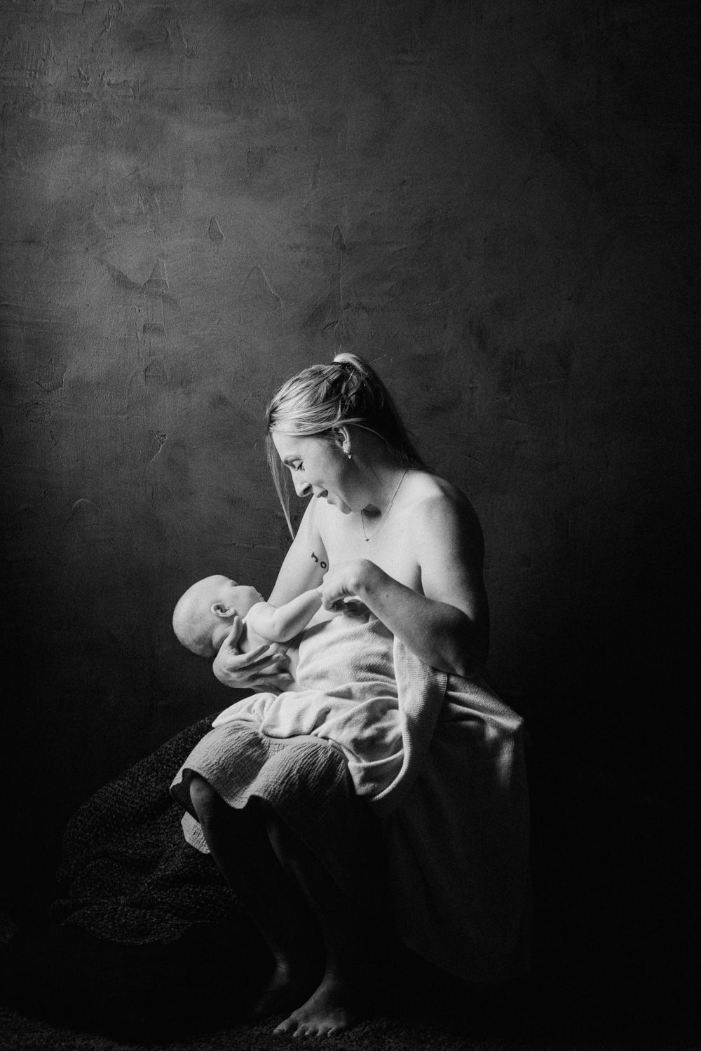 Black and white photo of a mother breastfeeding her newborn baby in a softly lit studio setting.