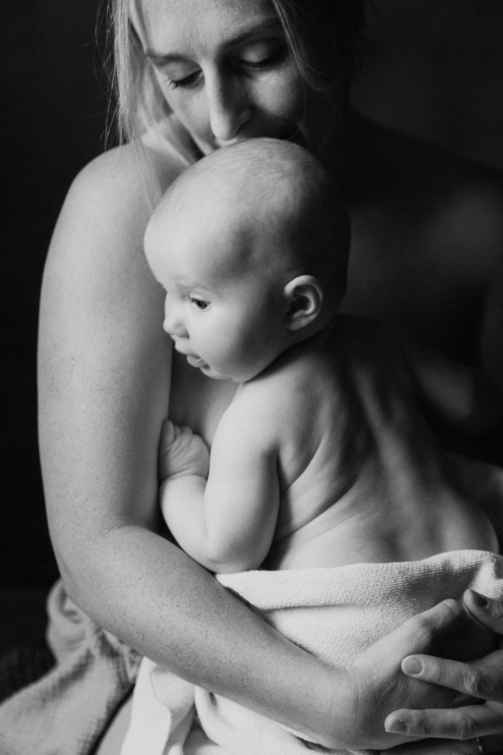 Black and white photo of a mother tenderly holding her newborn baby wrapped in a soft blanket.