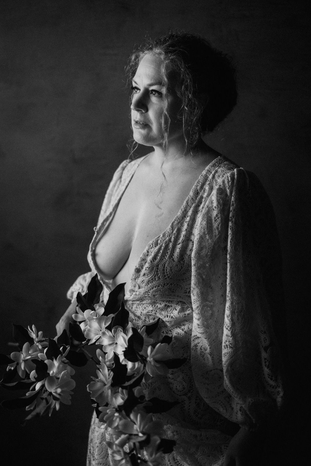 Black and white portrait of a woman in lace dress holding flowers, dramatic studio lighting.