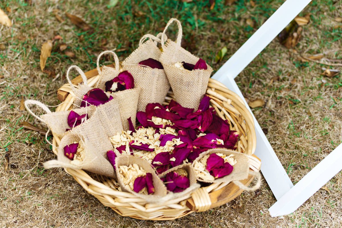 Burlap cones filled with magenta rose petals and white flowers arranged in a wicker basket for a wedding ceremony.