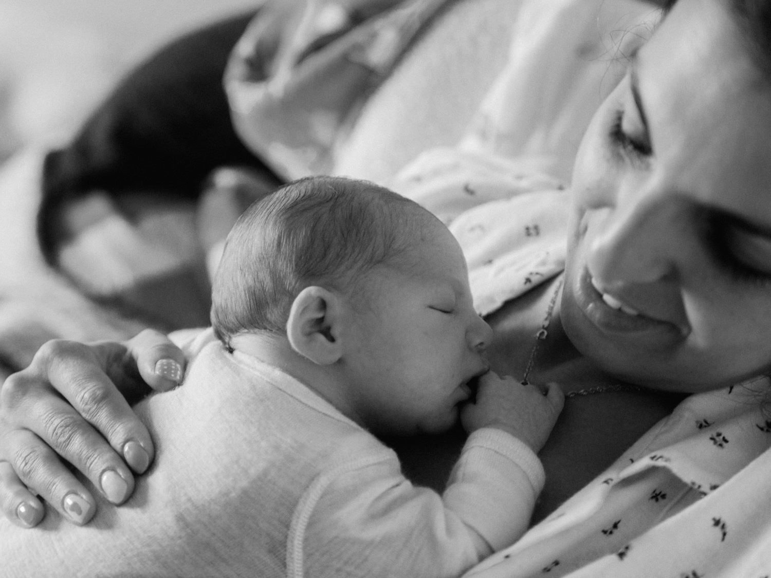Black and white photo of a newborn baby breastfeeding while a smiling mother looks on tenderly.