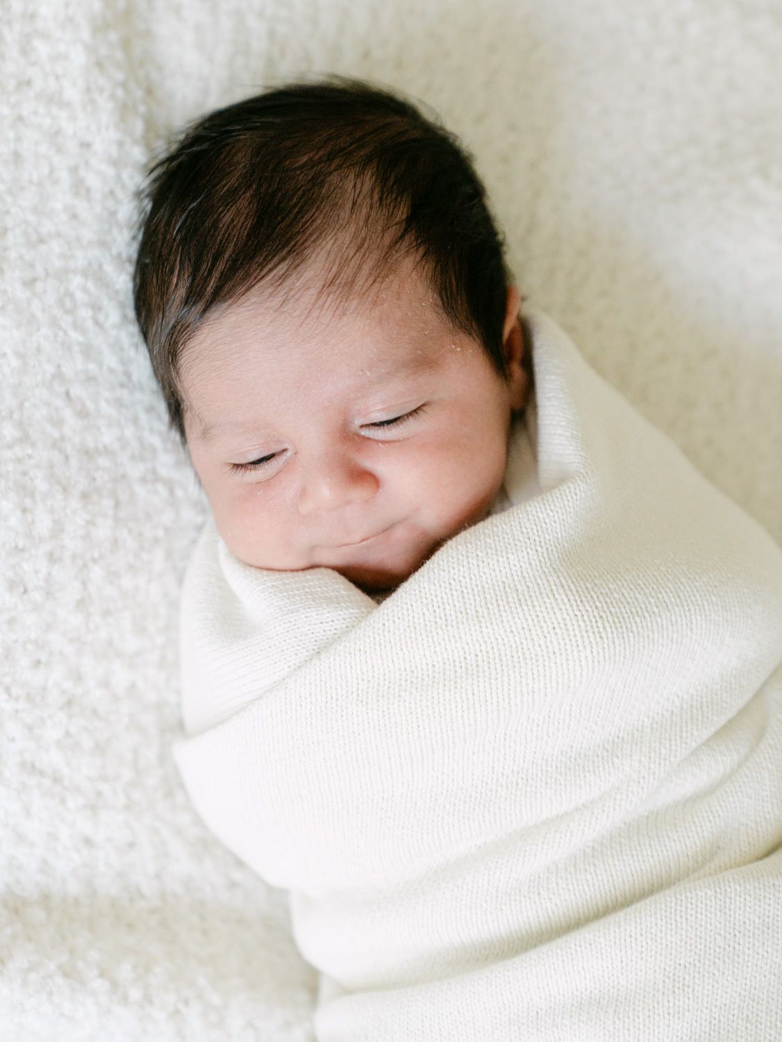Close-up of a peacefully sleeping swaddled newborn baby wrapped in cream blanket.