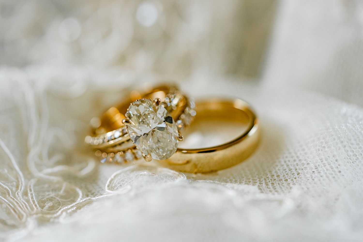 Gold wedding band and diamond engagement ring set displayed on white lace fabric.