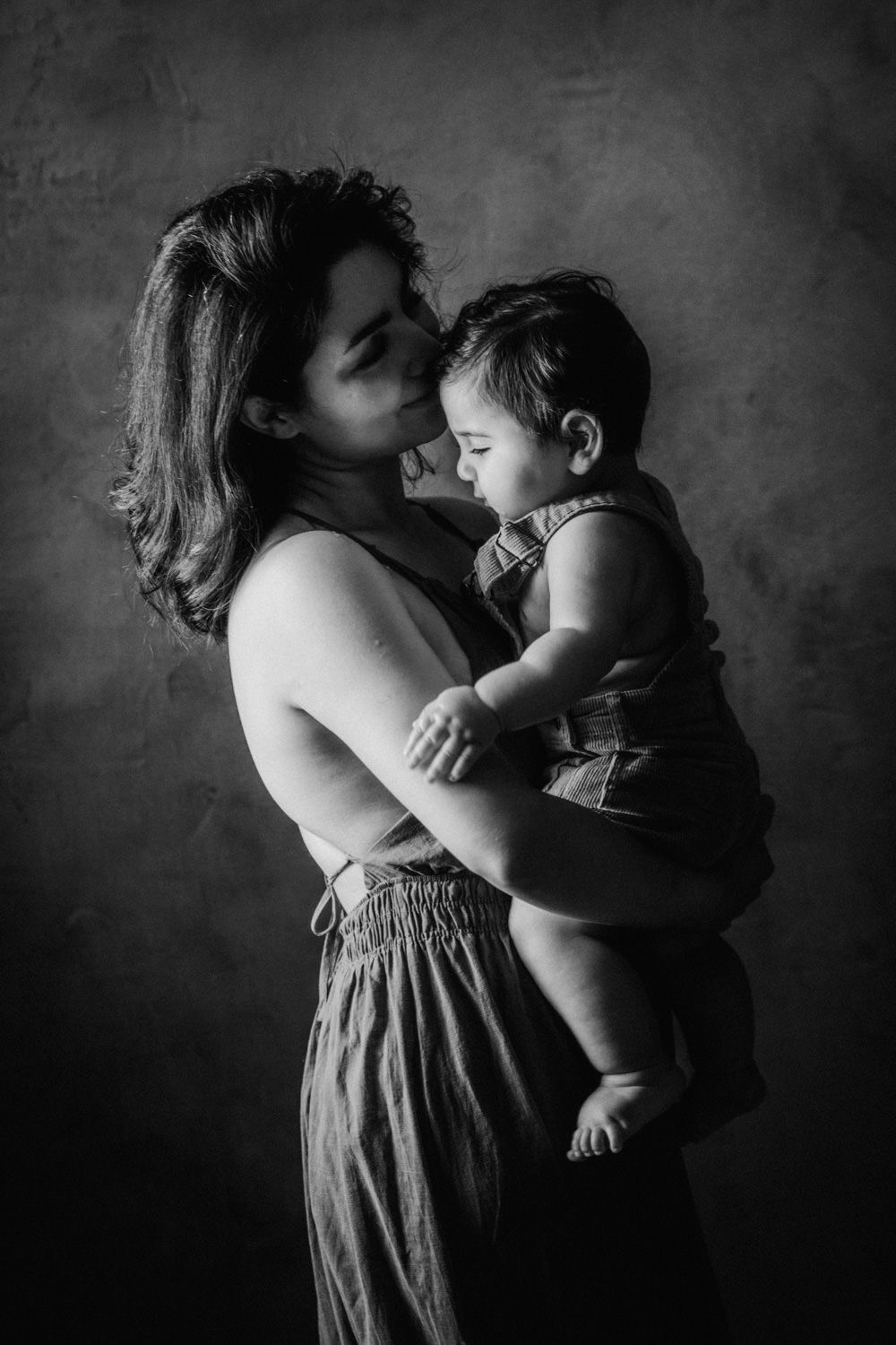 Black and white portrait of a mother tenderly kissing her baby, studio background.