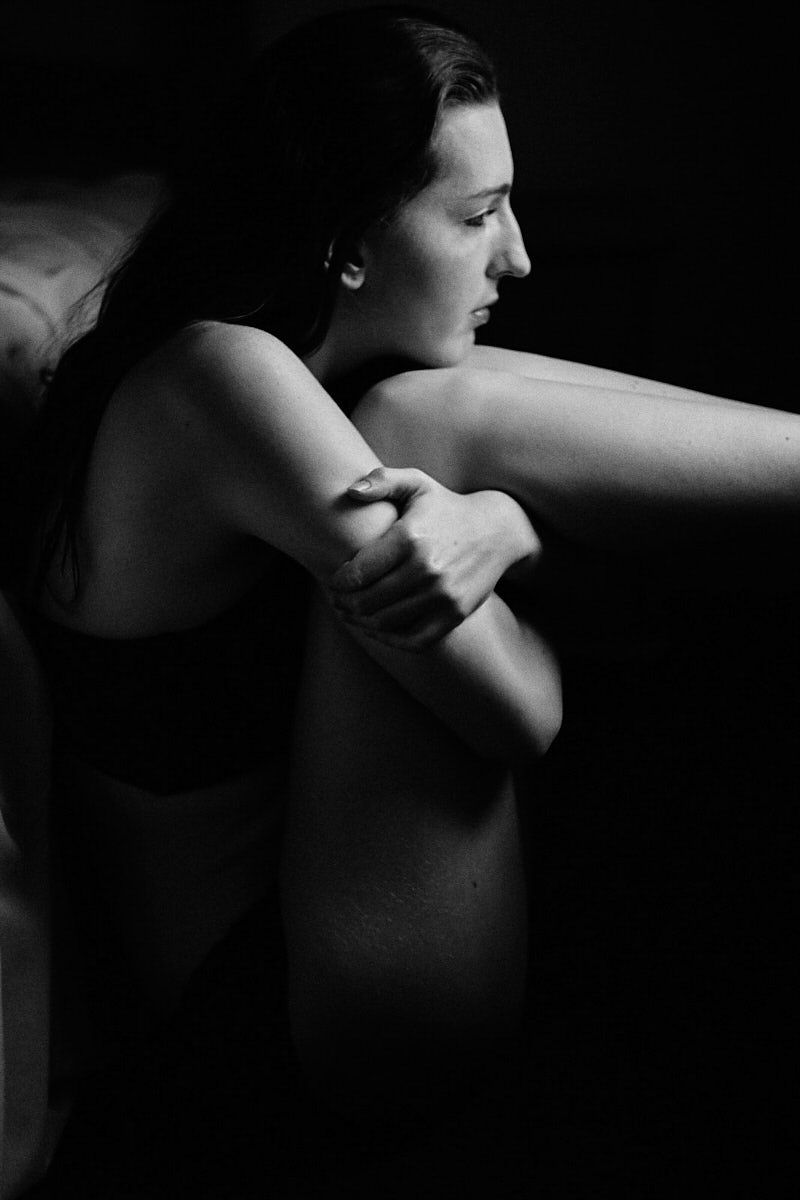 Black and white portrait of a woman hugging herself, captured in dramatic low-key lighting.