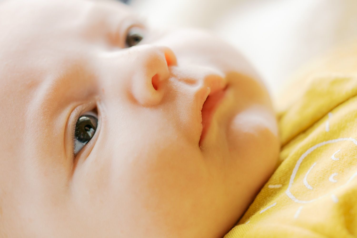 Close-up portrait of a curious baby with blue eyes looking upward, wearing a yellow outfit.