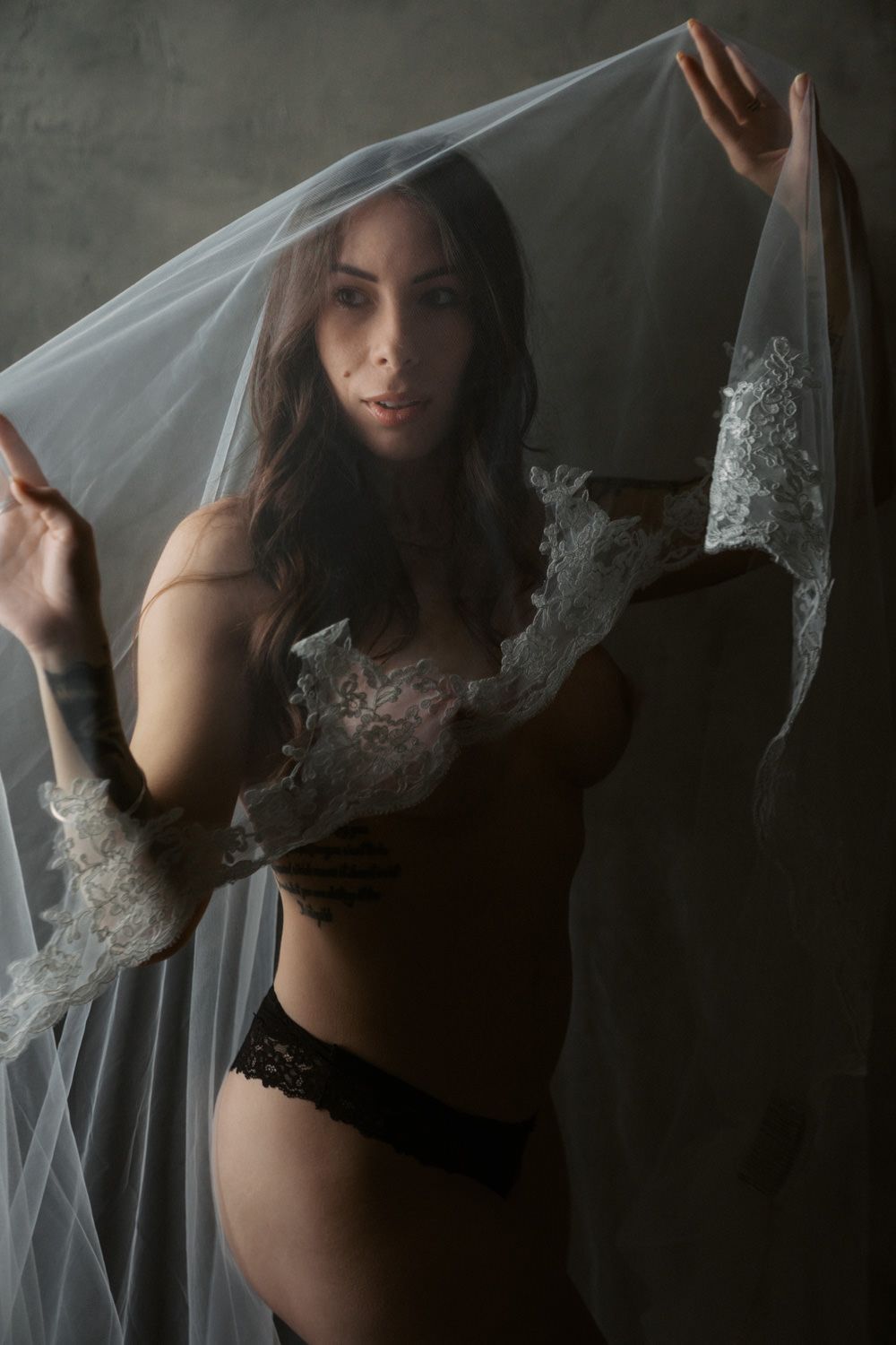 Woman in black lace lingerie holding a white bridal veil in a dramatic studio portrait.