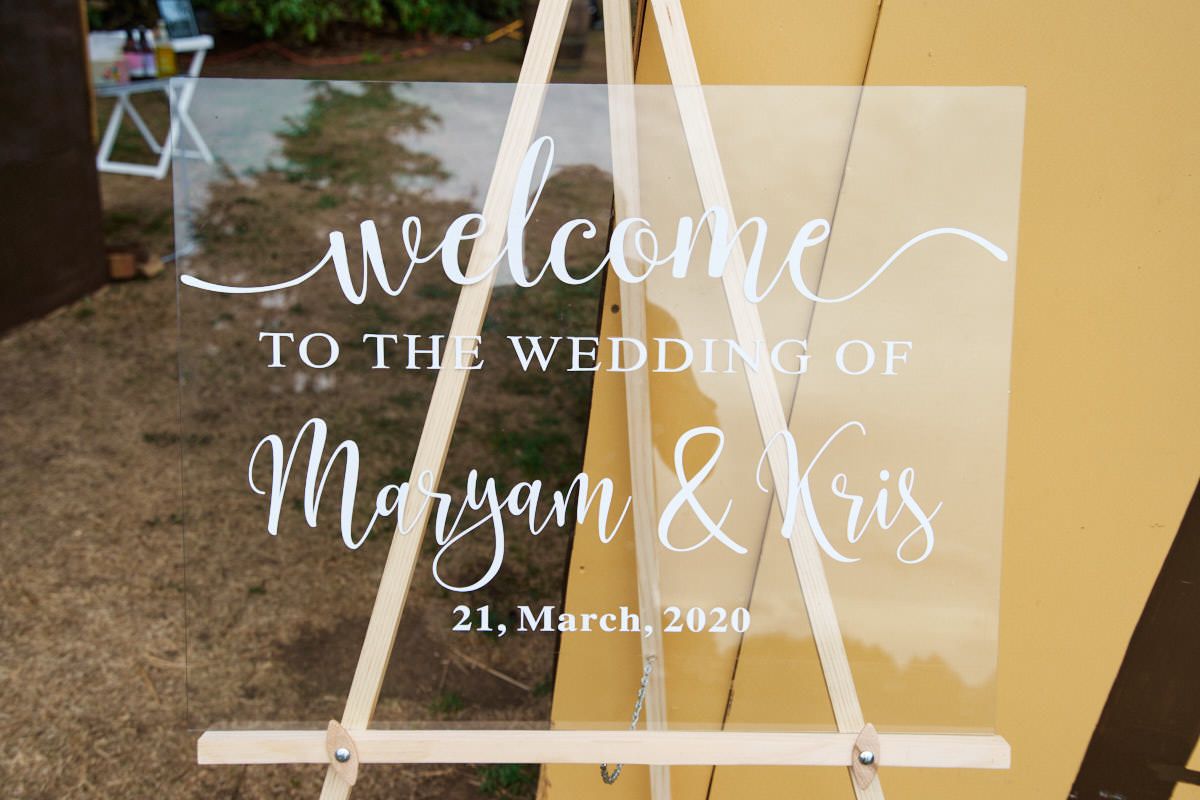 Elegant acrylic wedding welcome sign on wooden easel reading Welcome to the Wedding of Maryam & Kris, 21 March 2020.