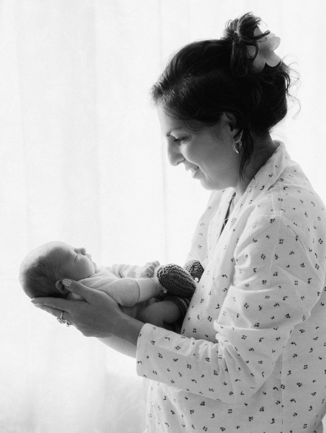 Black and white photo of a mother tenderly holding her newborn baby near a bright window.