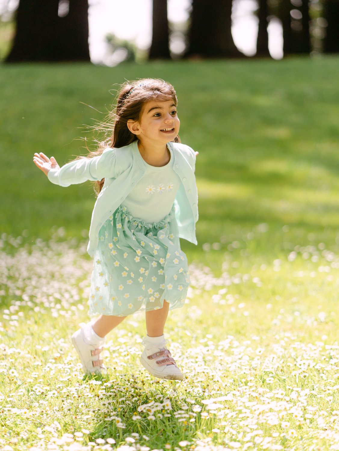A joyful young girl in a mint green outfit runs through a sunny daisy field, her hair flowing in the breeze.