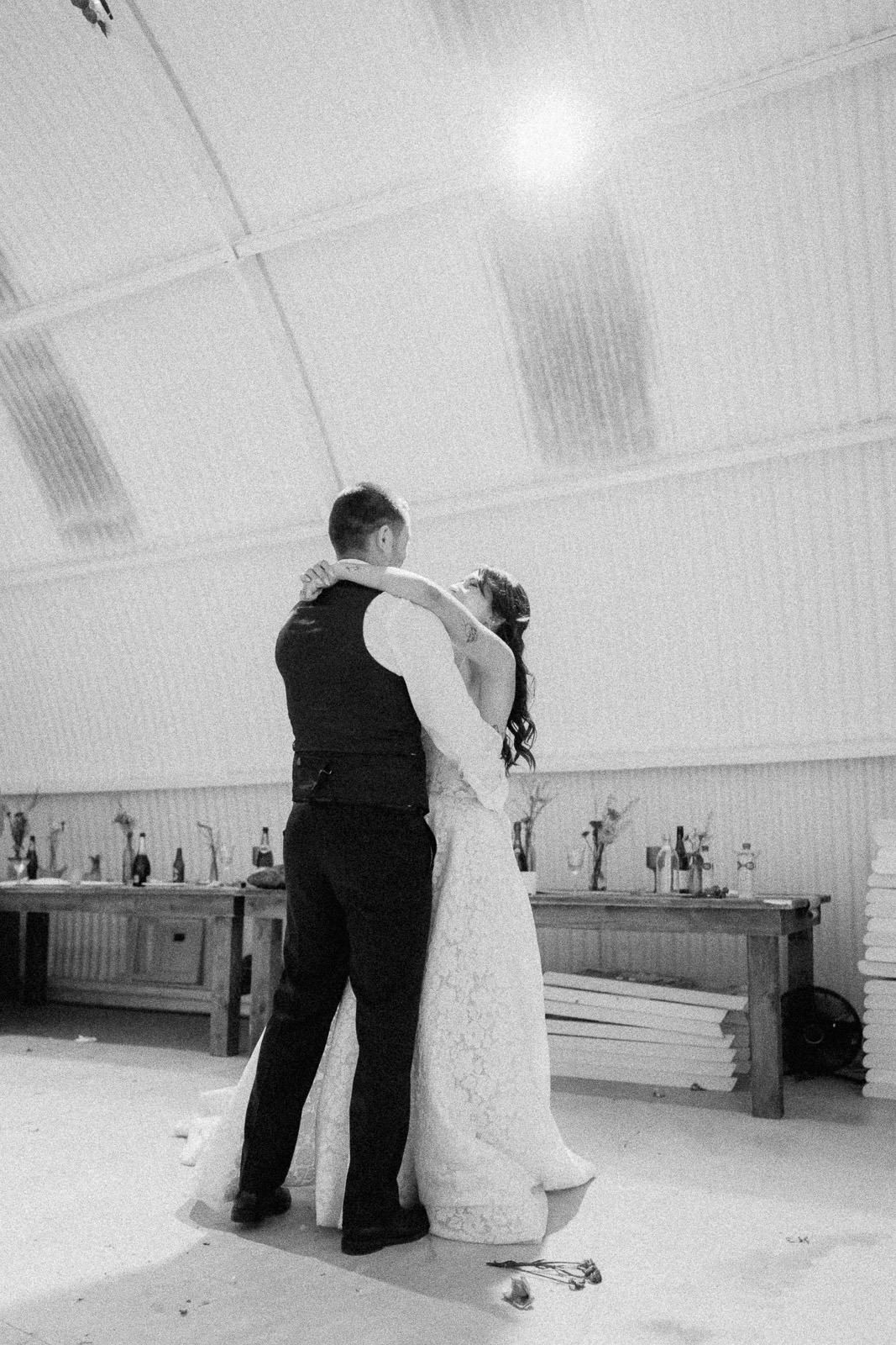 Black and white photo of bride and groom sharing their first dance in a rustic barn wedding venue.