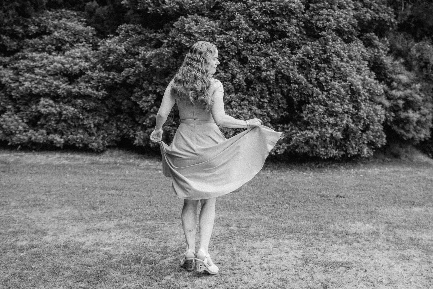 Black and white photo of a woman in a flowing dress twirling in a lush green garden.