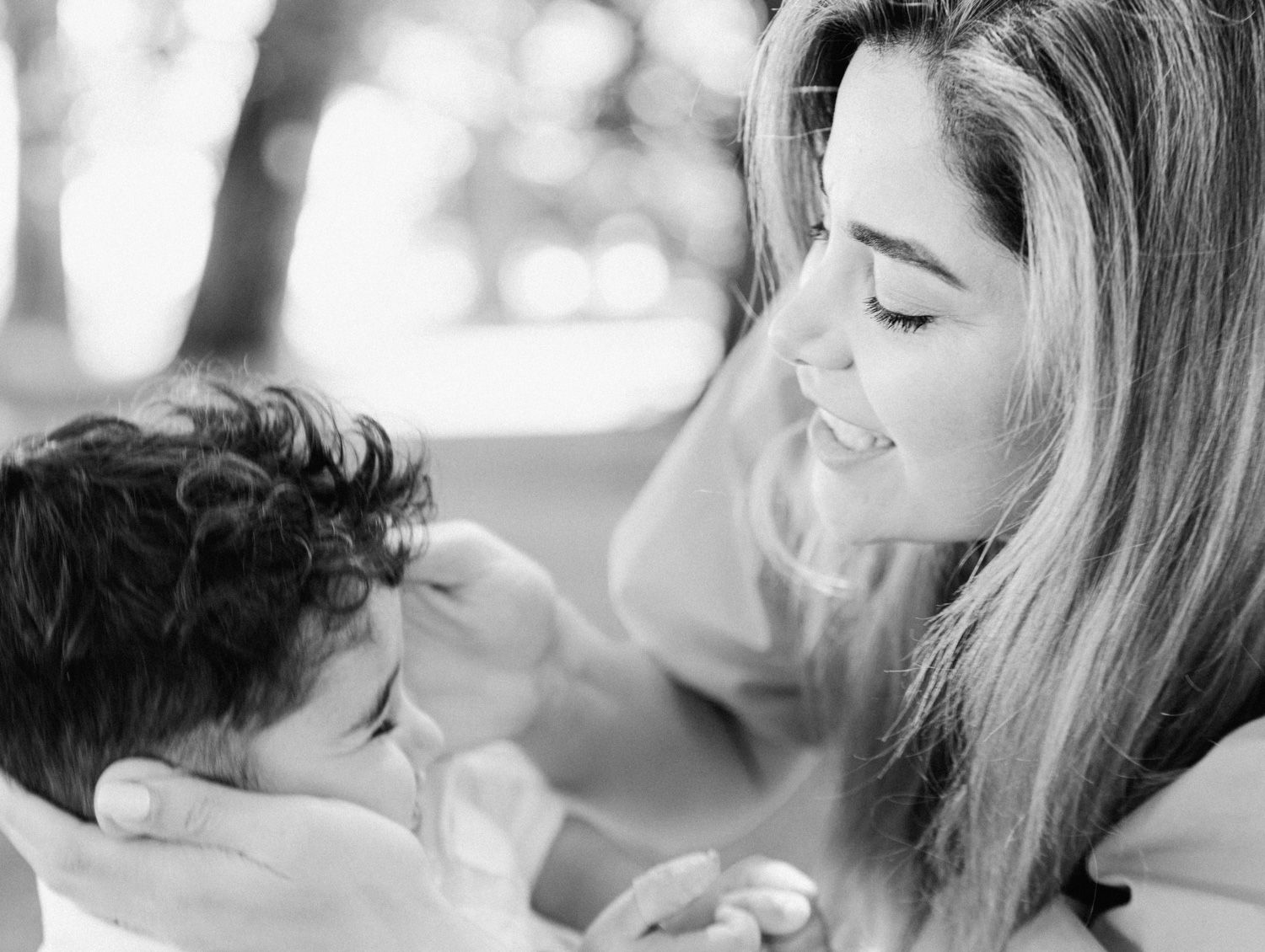 Black and white photo of a smiling woman tenderly holding and gazing at a young child outdoors.