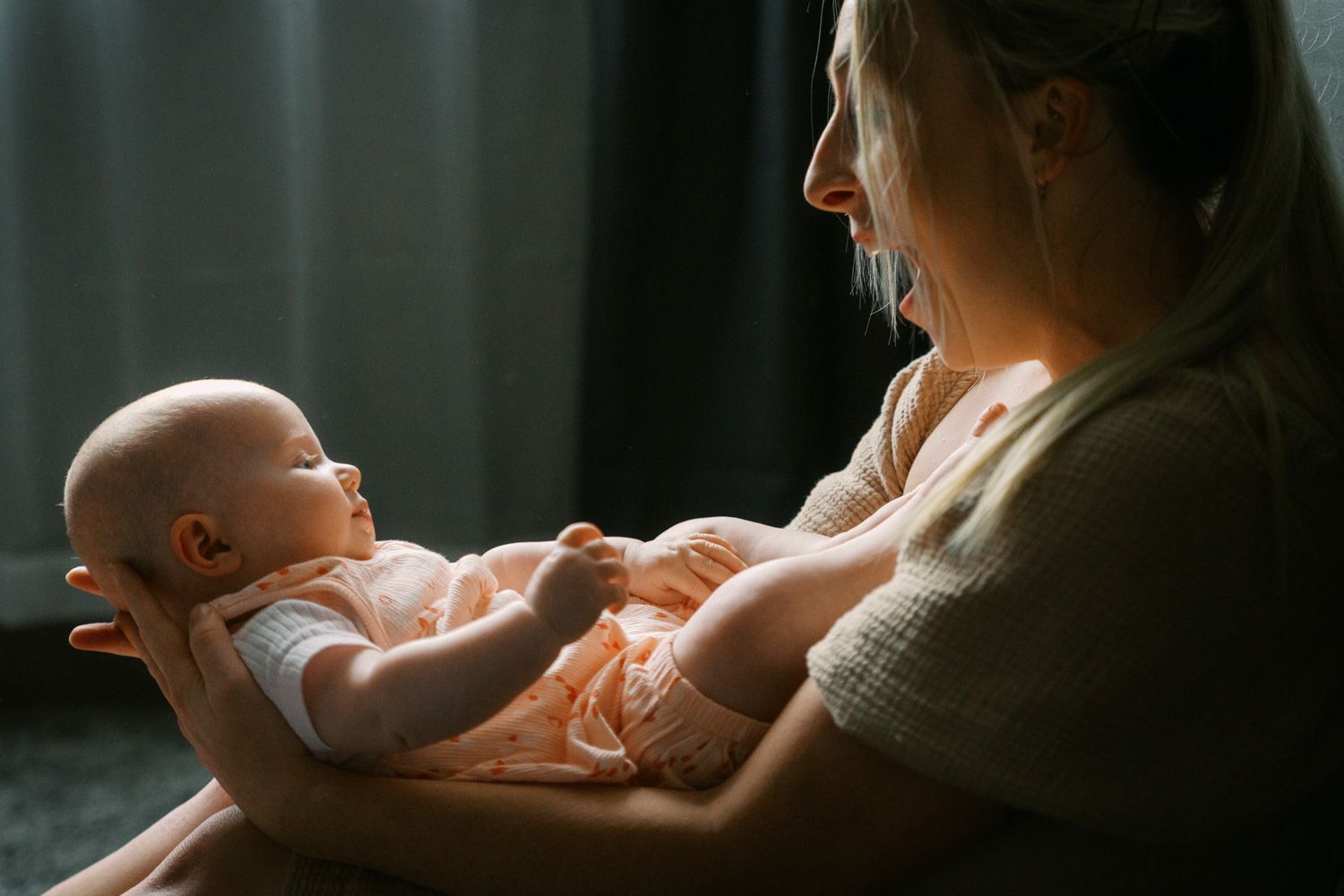 A mother tenderly holds her newborn baby in soft, warm light near a window.