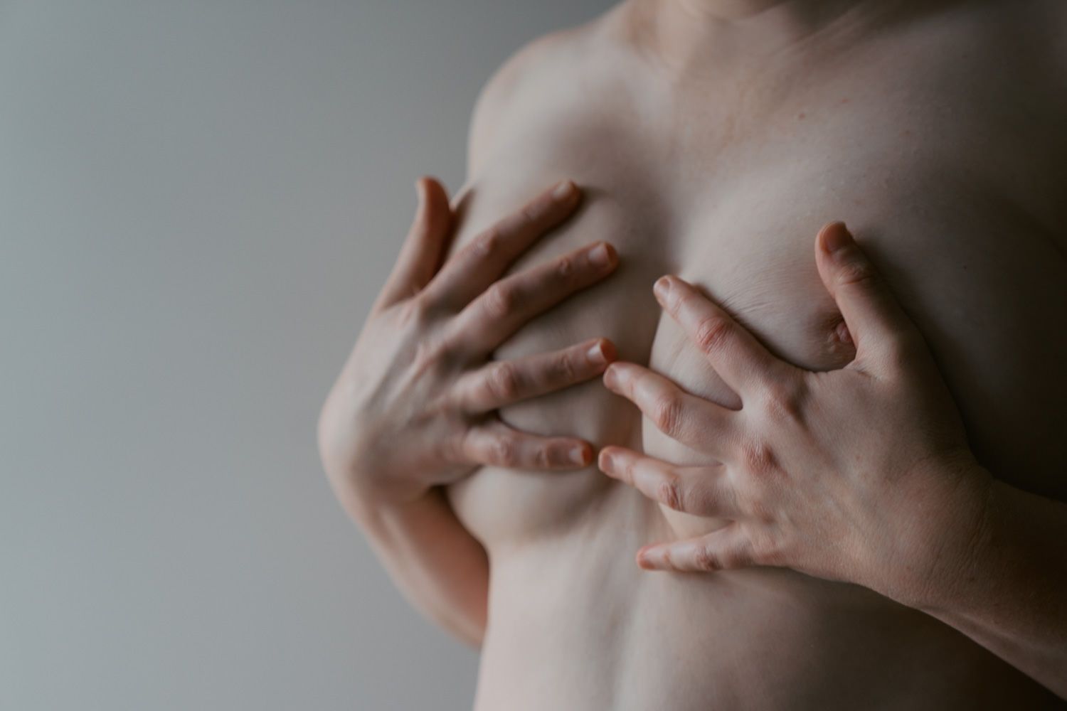 Person performing a breast self-examination with both hands on chest for health awareness.