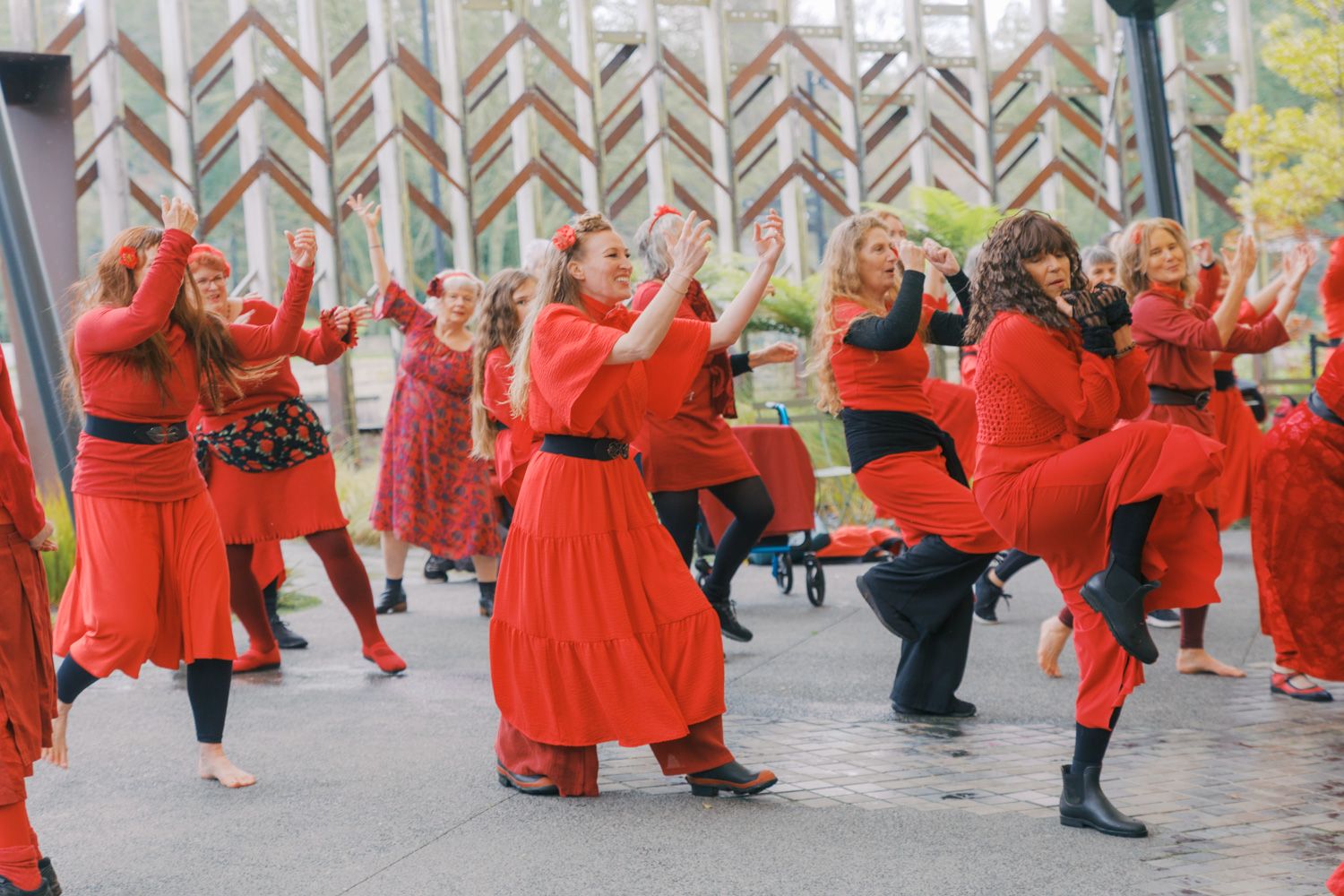 Group of women in red costumes performing a traditional folk dance outdoors at a cultural festival.