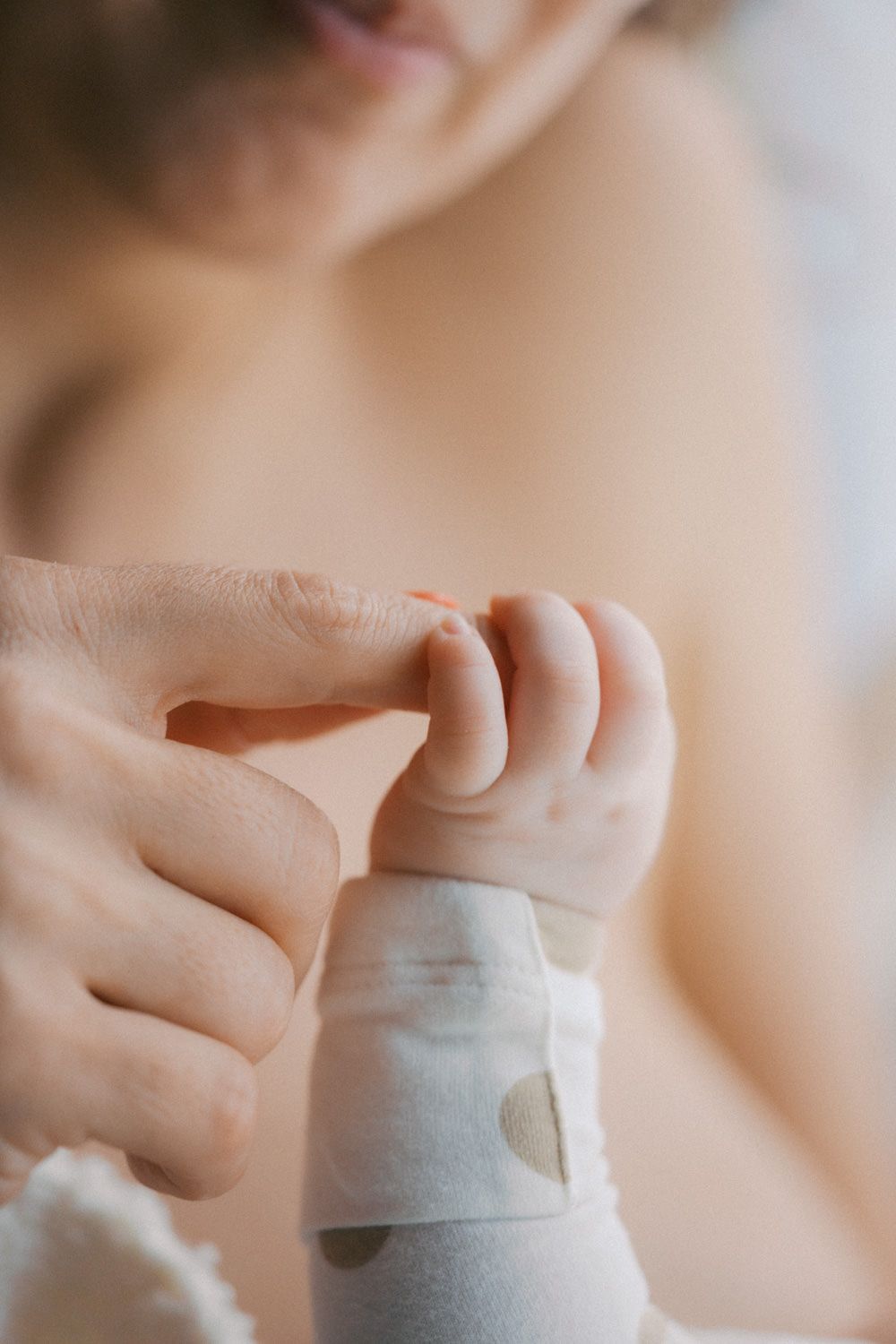 Close-up of a newborn baby grasping an adult's finger, wearing a polka dot onesie.