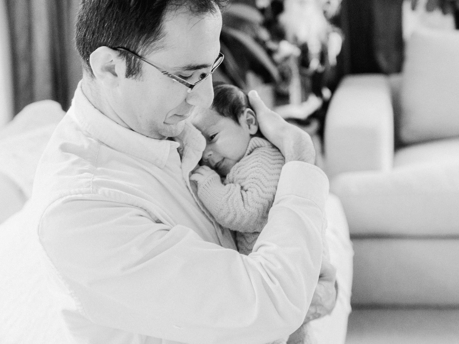 Black and white photo of a father tenderly holding his sleeping newborn baby close to his chest.
