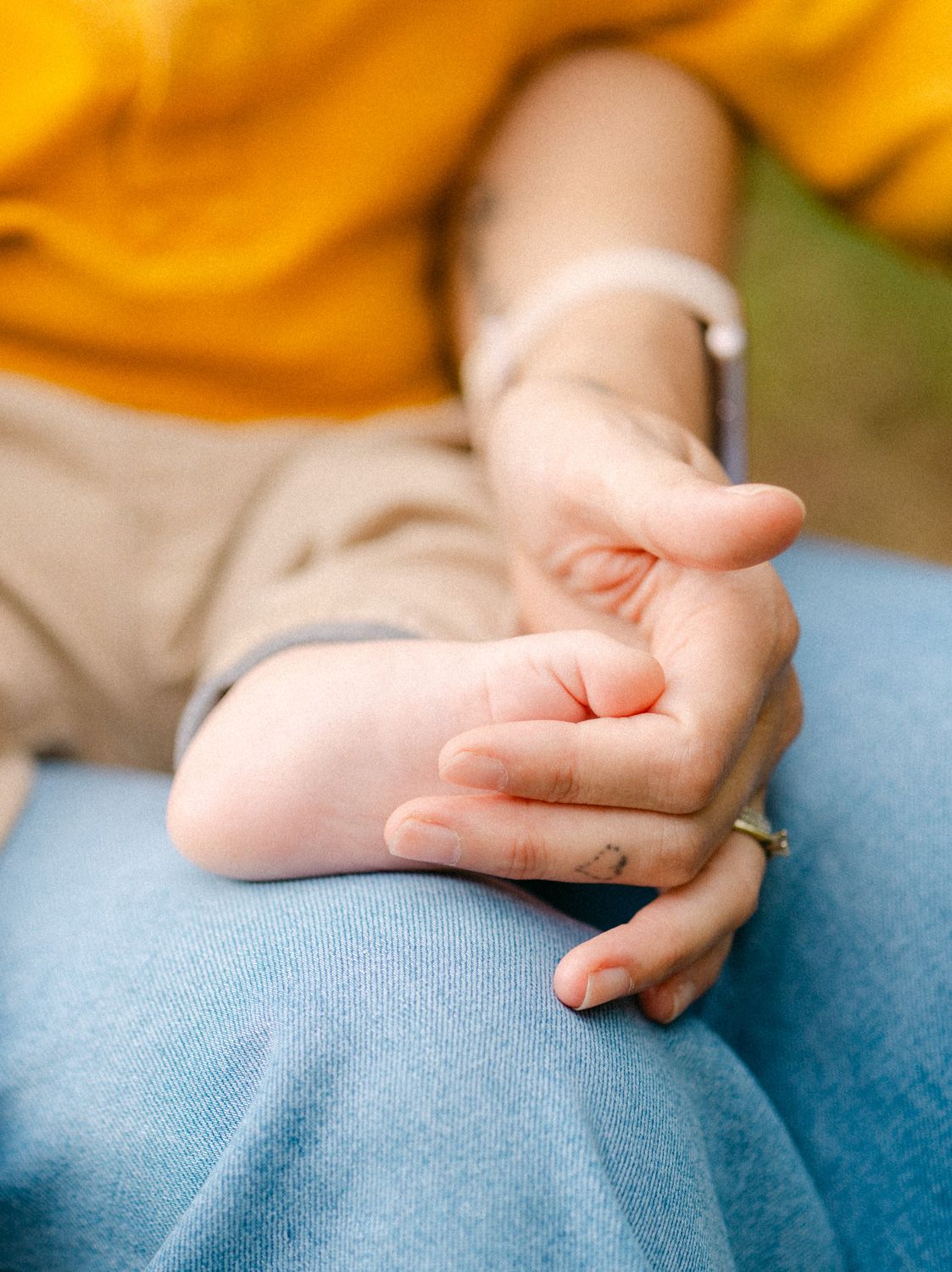 Close-up of two hands gently clasped together, wearing a ring and bracelet, resting on blue jeans.