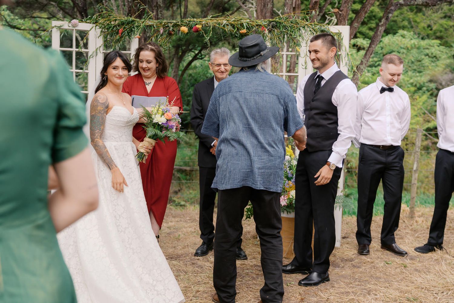 Bride and groom share a joyful moment at an outdoor wedding ceremony with guests and officiant surrounded by greenery.
